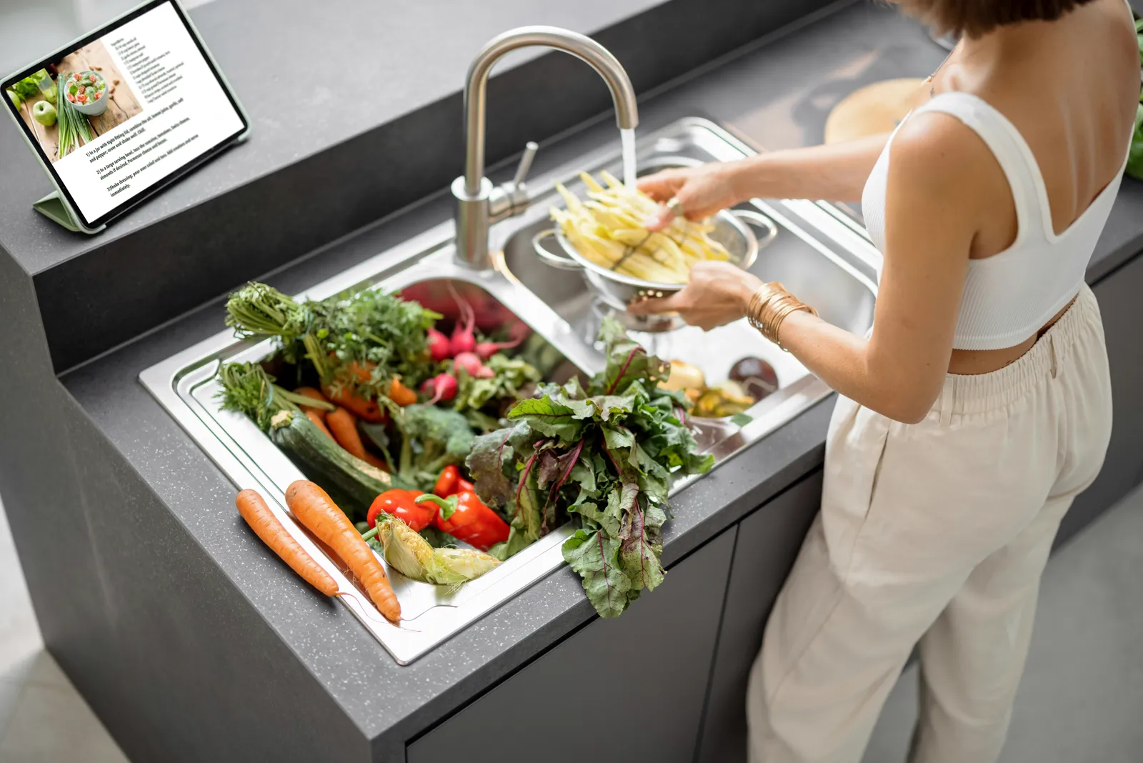 Woman washing fresh vegetables at a modern kitchen sink with a large professional-style faucet — water quality affects everything you rinse and cook